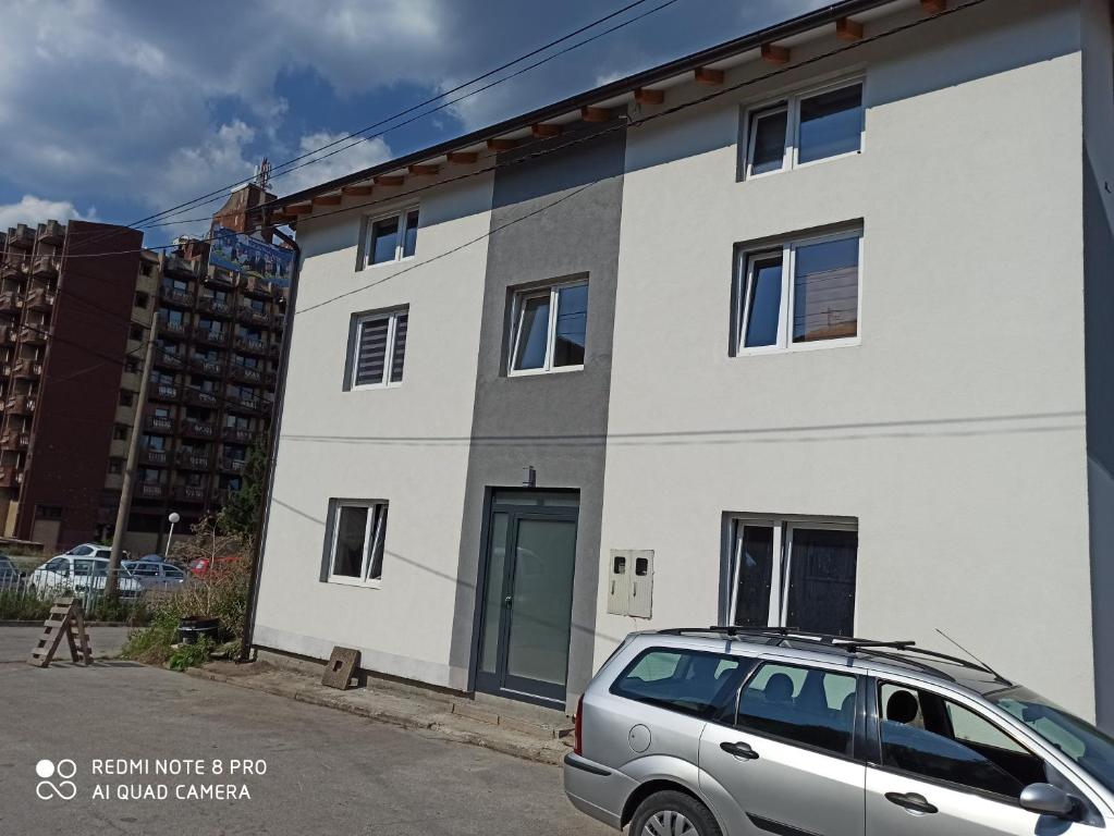 een wit gebouw met een auto ervoor geparkeerd bij Apartmani Kula in Tuzla