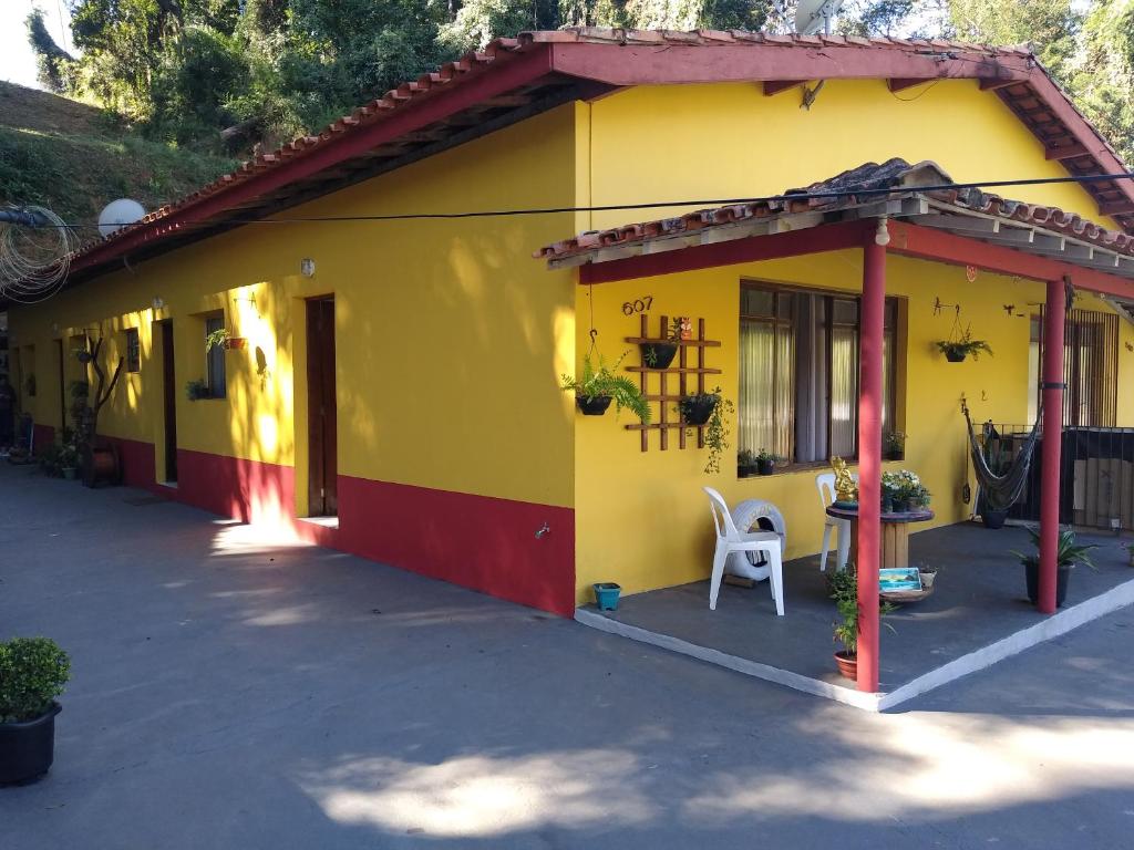 uma casa amarela e vermelha com uma cadeira branca lá fora em Recanto Só Alegria. em Serra Negra