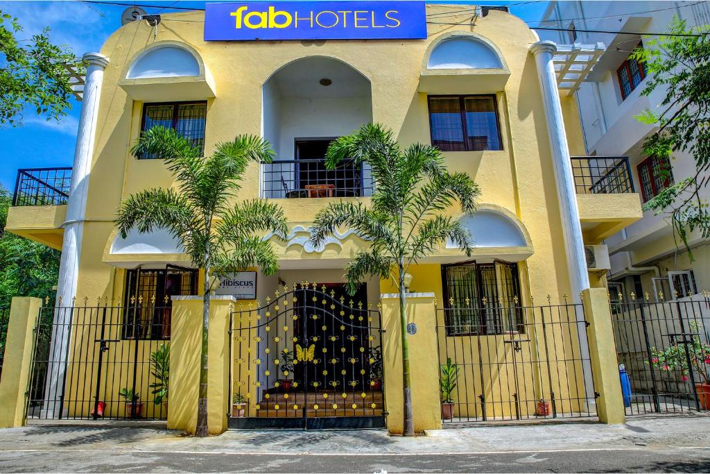 a yellow building with palm trees in front of it at FabHotel Hibiscus Stays in Chennai