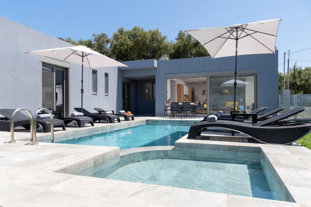 a house with a swimming pool with chairs and an umbrella at Villa Ampela by PosarelliVillas in Agia Marina Nea Kydonias