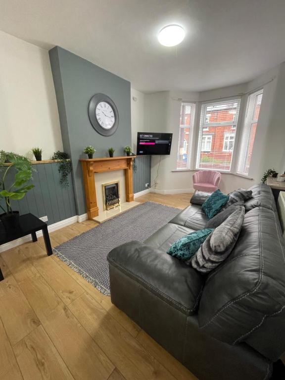 a living room with a leather couch and a clock at Bentley Place in Crewe