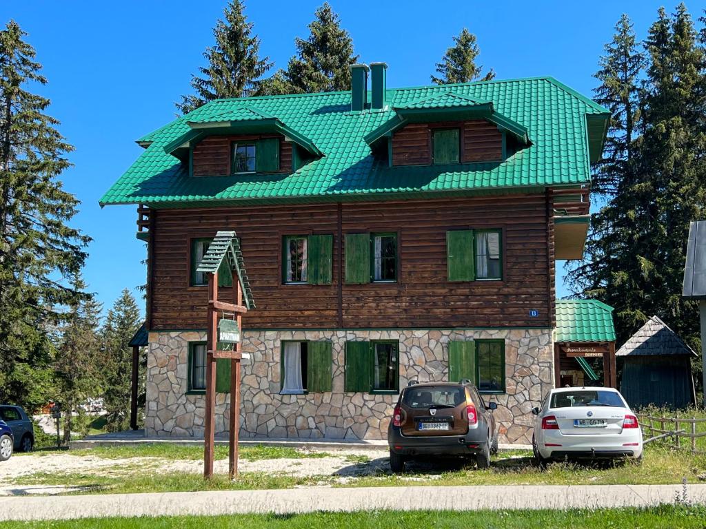 uma casa com um telhado verde e dois carros estacionados na frente em Dormire Apartmans em Žabljak