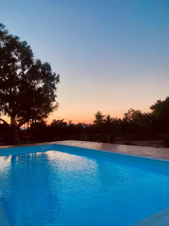 a blue swimming pool with a sunset in the background at Seaside "Stone & Light Villa II" close to Aegina City in Khlóï