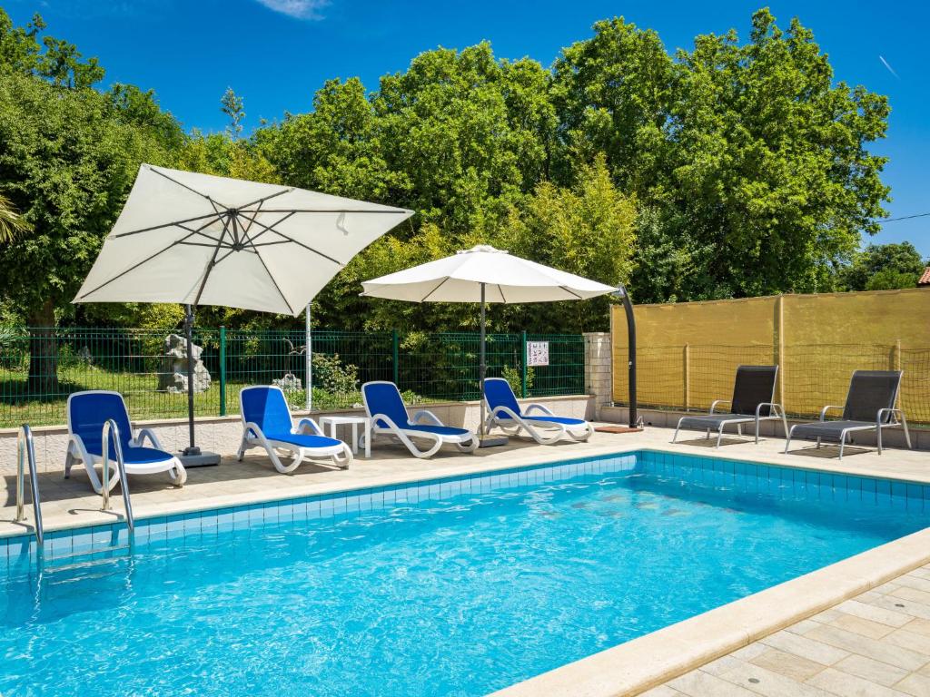 a swimming pool with blue chairs and umbrellas at Holiday Home Verbanac - LBN351 by Interhome in Labin