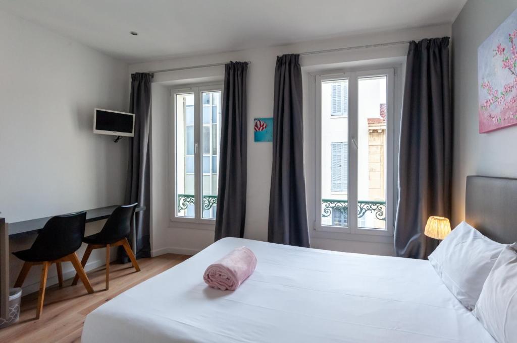 a bedroom with a white bed and two windows at Hotel l'Hotera in Cannes