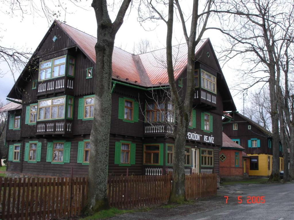 una grande casa in legno con finestre verdi e una recinzione di Penzion Rejviz a Rejvíz