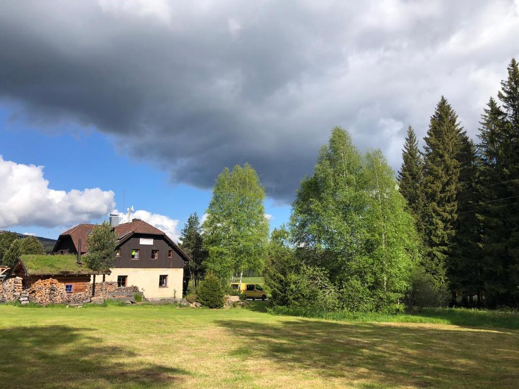 ein Haus auf einem Feld mit Bäumen im Hintergrund in der Unterkunft Penzion ''Pod Hůreckým vrchem'' in Prášily