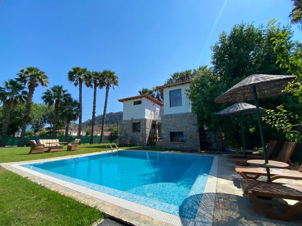 a pool with chairs and an umbrella and a house at Villa Merry - Dalyan Stonehouse with Palmtrees, 50m to River in Ortaca