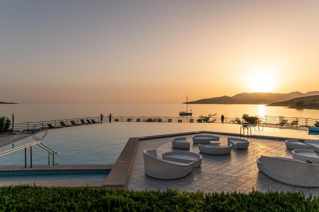 uma piscina com cadeiras e o oceano ao pôr do sol em Aparthotel Plat em Mlini