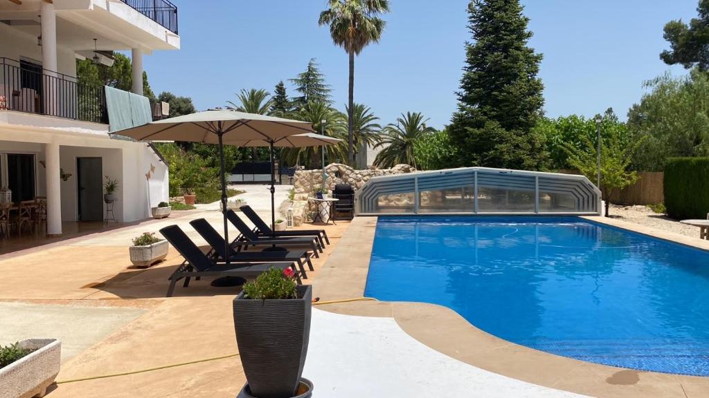 una piscina con sillas y una sombrilla junto a un edificio en B&B Casa Mil Sueños, en Ontinyent