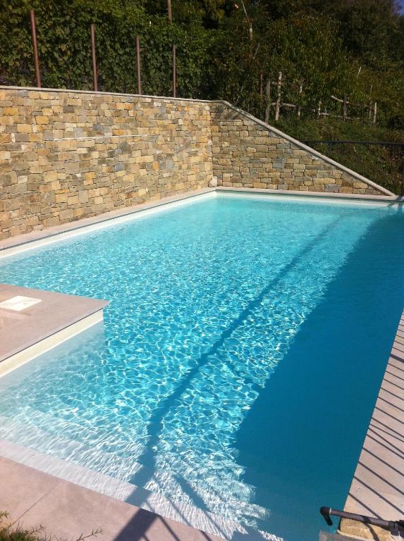 a large blue swimming pool with a brick wall at La Vigna Del Parroco in Verduno