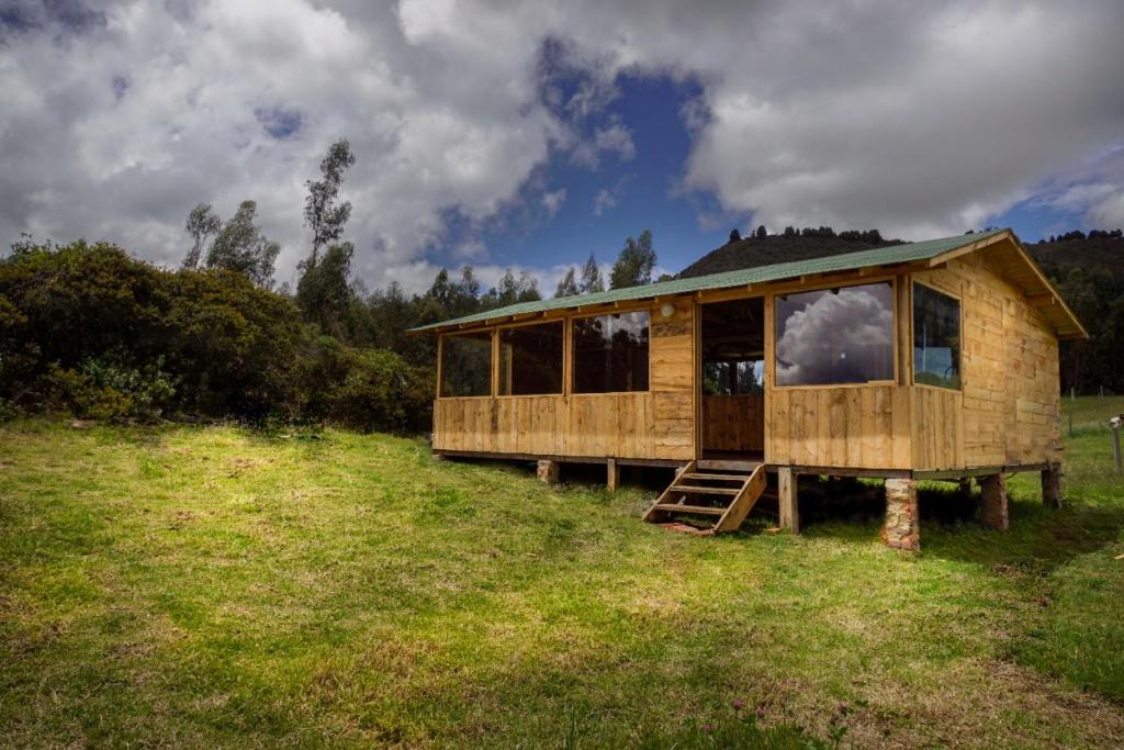 a wooden cabin in a grassy field with a sky at Villa Maria in Guatavita