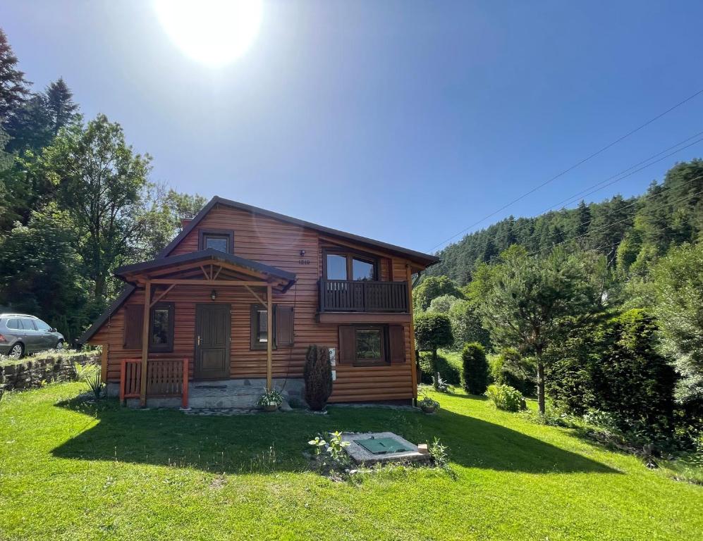 a wooden house on a grassy yard with the sun in the sky at Chata Zahura in Spišské Vlachy