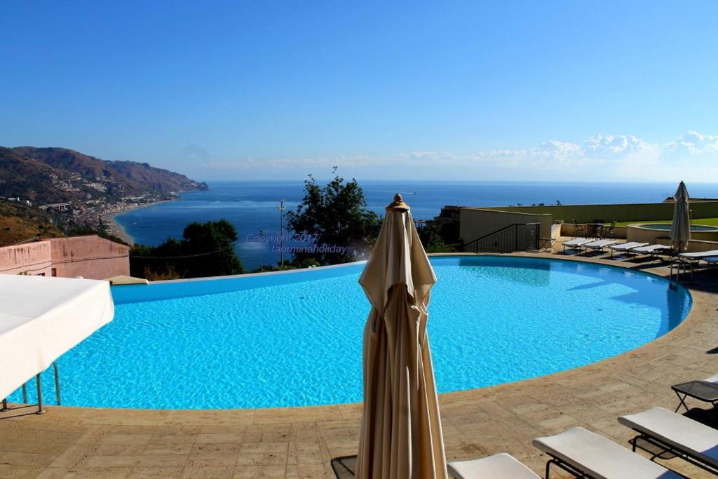 a large swimming pool with an umbrella next to the ocean at Taormina Helas Apartment by Taormina Holidays in Taormina
