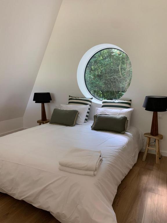 a bedroom with a large white bed with a large window at La Maison Villeneuve - Lodges avec bains nordiques in Donnay