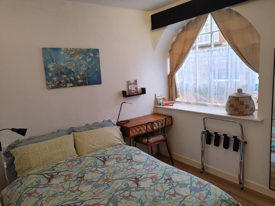 a bedroom with a bed and a table and a window at Cosy Flat in a Pretty Town. in Crewkerne