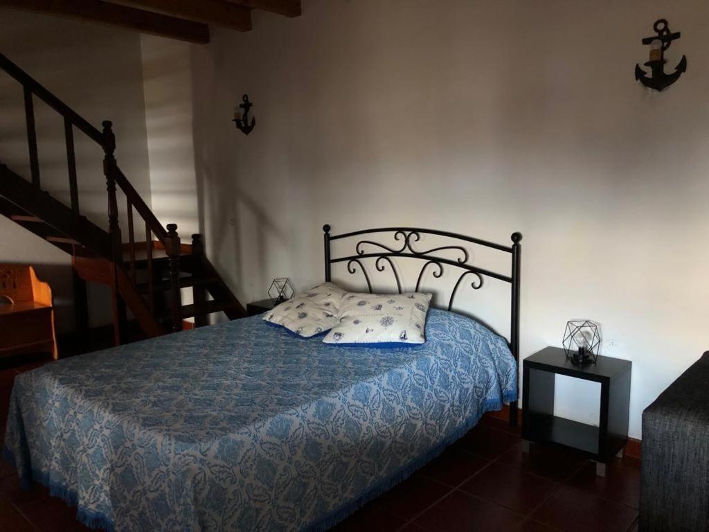 a bedroom with a bed with a blue comforter and a staircase at Adega do Golfinho in Feiteira