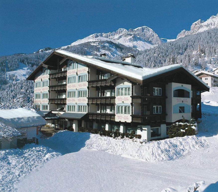 un gran edificio en la nieve con montañas en el fondo en Alpen Hotel Corona, en Vigo di Fassa