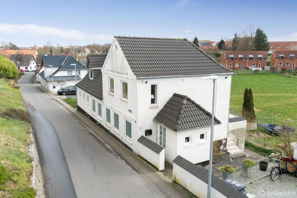 a white house with a black roof on a street at 210 m2 hus med plads til 8 gæster in Nordborg