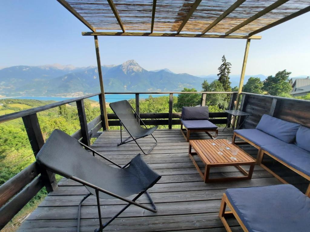 une terrasse en bois avec des chaises, un canapé et une table dans l'établissement Chalet bioclimatique avec vue sur le lac de Serre Ponçon, à Saint-Apollinaire