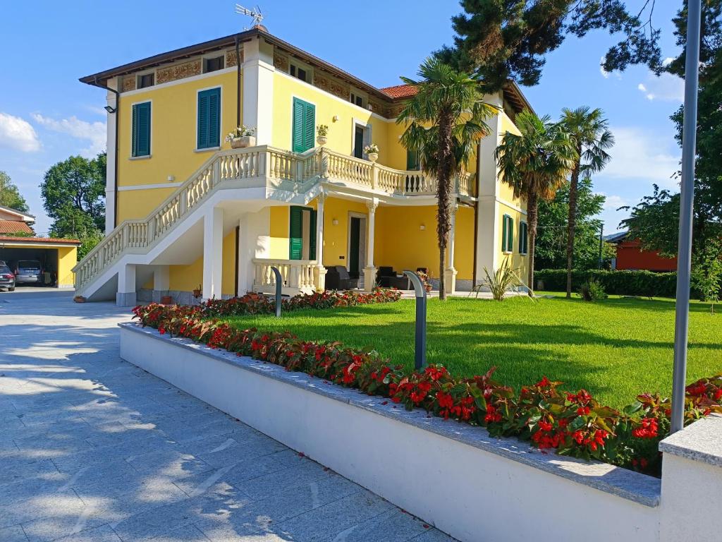 una casa gialla con fiori rossi in un cortile di B&B VILLA PREZIOSA LAGO MAGGIORE a Lesa