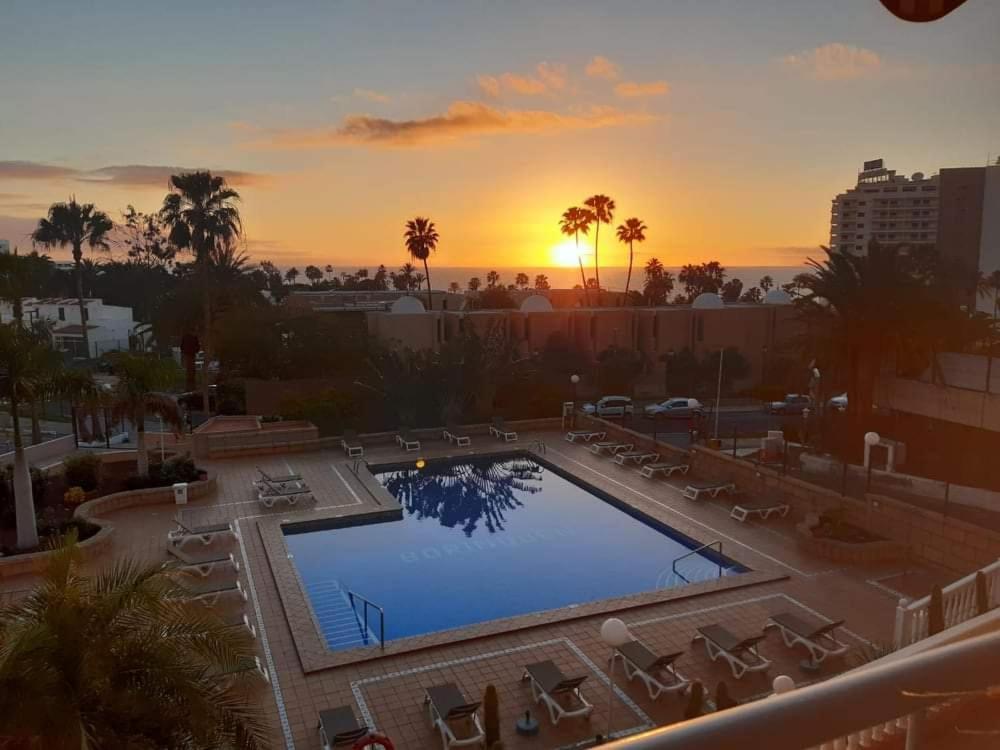 een zwembad met stoelen en een zonsondergang op de achtergrond bij Borinquen Sky Apartments in Playa de las Americas