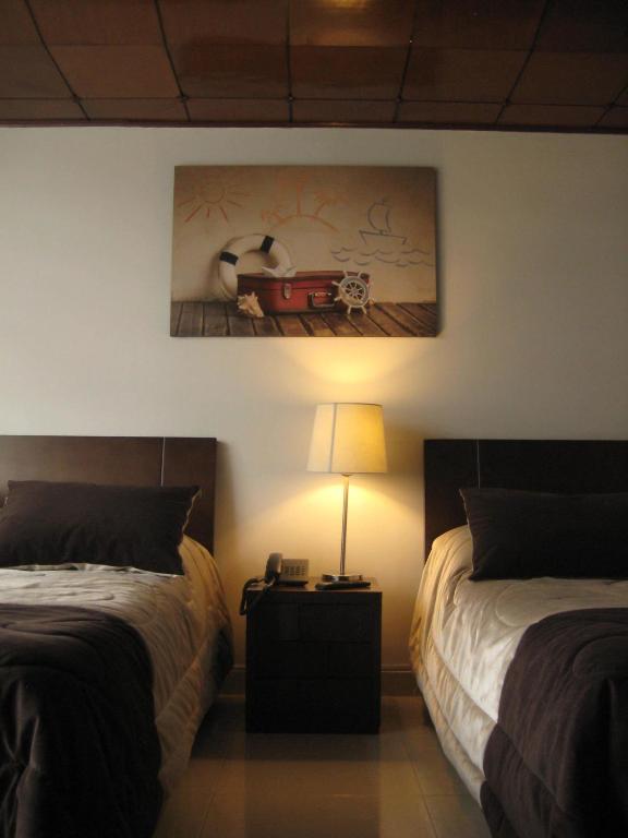 a bedroom with two beds and a lamp and a painting at Hotel Casa Santa Marta in Bogotá