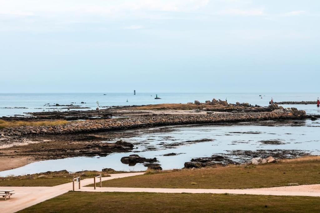 een uitzicht op een strand met een bank en het water bij APPART-DUPLEX VUE MER PANORAMIQUE BALCON & PISCINE proche commerce in Penmarcʼh