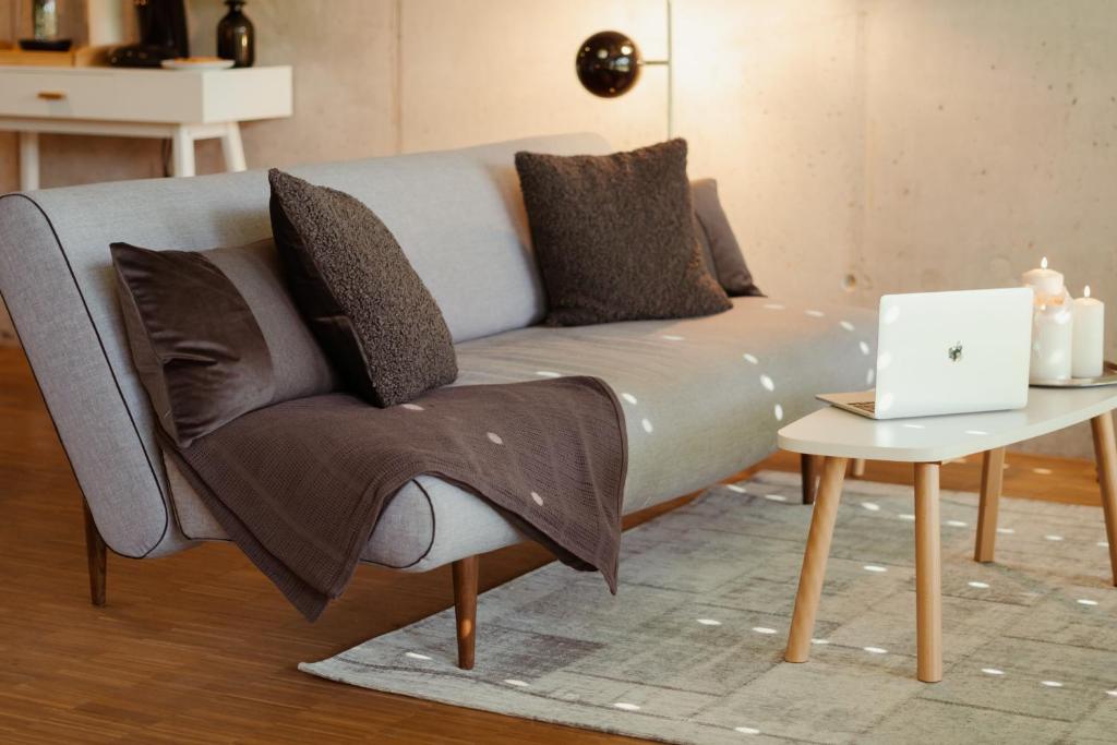 ein Sofa mit Kissen und ein Laptop auf einem Tisch in der Unterkunft Loft-Apartment - Bestlage am Kurpark mit Terrasse - kostenloses Parken - Küche - Netflix - Waschmaschine in Wiesbaden