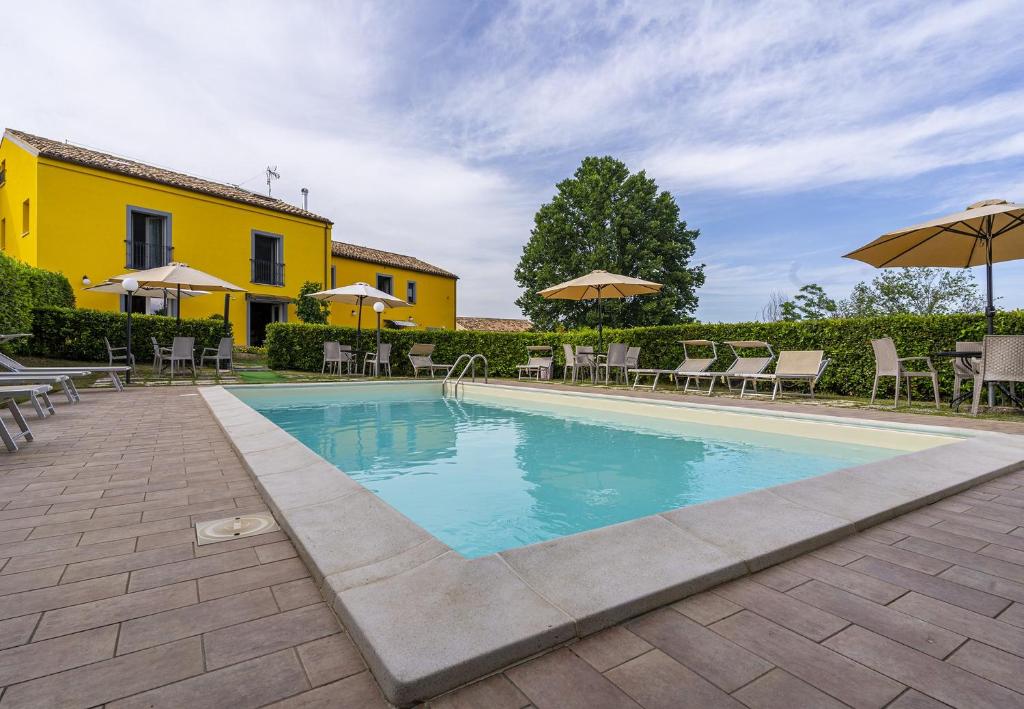 basen z leżakami i parasolami obok żółtego budynku w obiekcie L'Olmo di Casigliano w mieście Cessapalombo