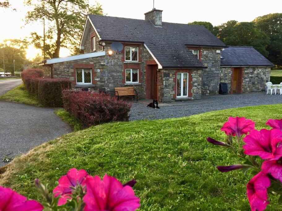 a stone house with pink flowers in front of it at Dan Rua's Cottage in Cavan