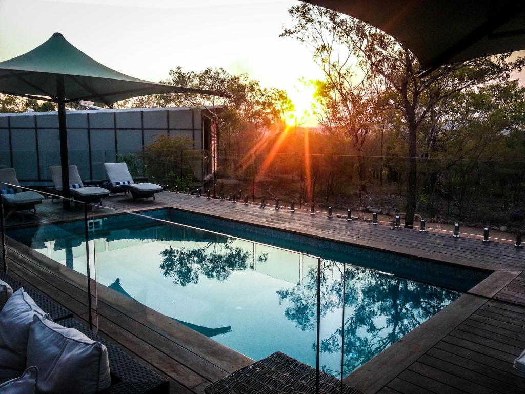 a swimming pool with a sunset in the background at Cicada Lodge in Katherine