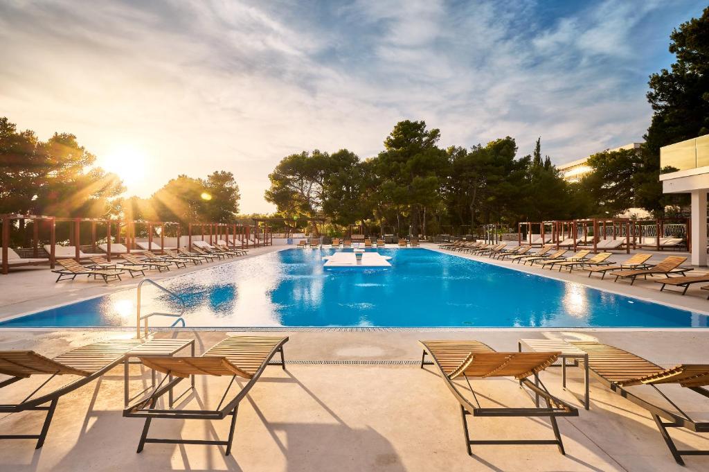 a large swimming pool with chairs and the sun setting at Hotel Imperial in Vodice