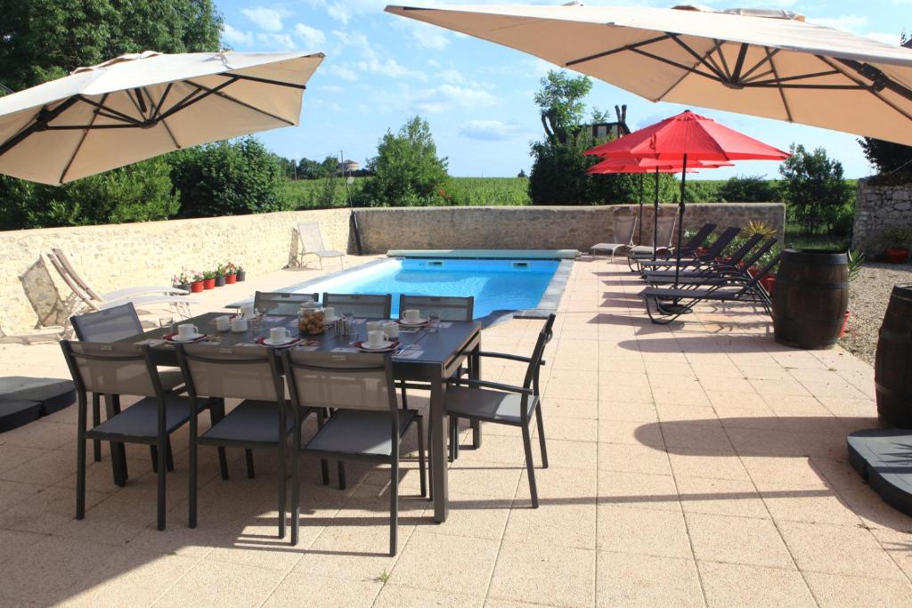 a table with chairs and umbrellas next to a pool at Chambres d'hôtes La Fontaine! in Saint-Seurin-de-Cadourne