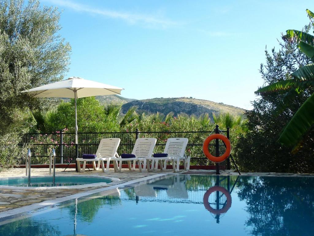 een groep stoelen en een parasol naast een zwembad bij Villa Poseidon in Kateliós