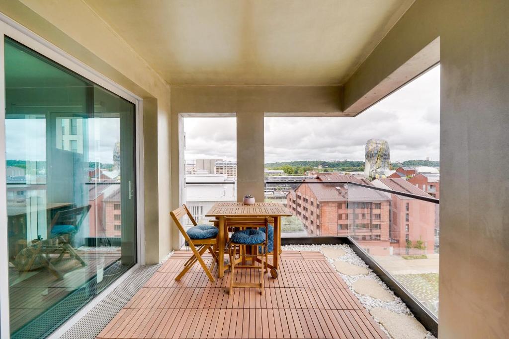 einen Balkon mit einem Holztisch und Stühlen sowie einem Fenster in der Unterkunft L'EMBLEM - Incroyable vue sur la Cité du vin in Bordeaux