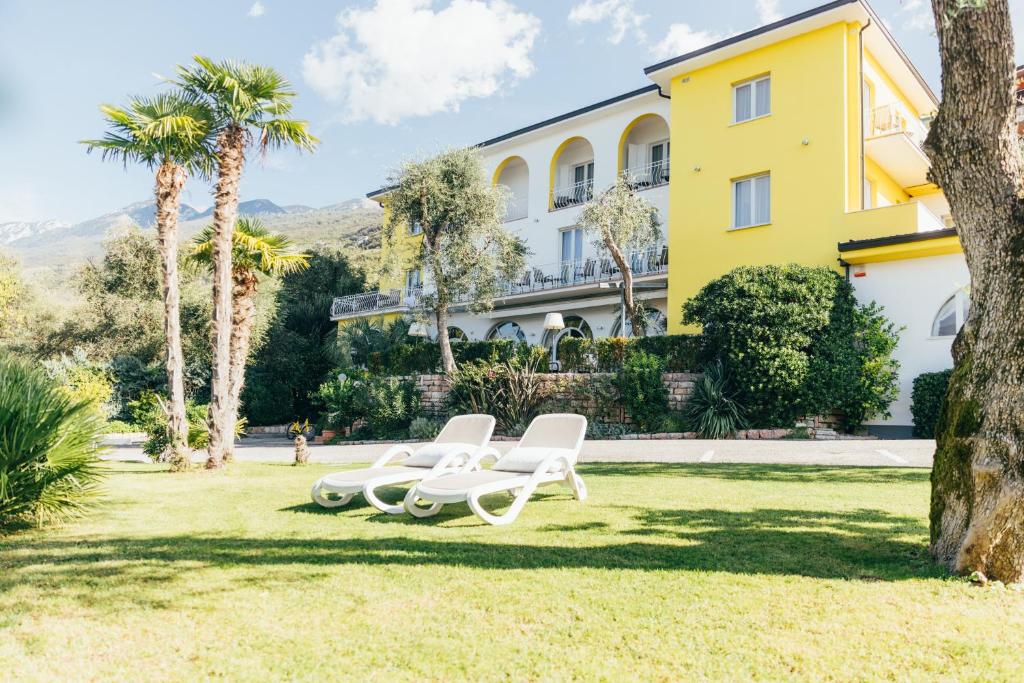 un bâtiment jaune avec deux chaises blanches et des palmiers dans l'établissement Hotel Orione - Lake Front Hotel, à Brenzone