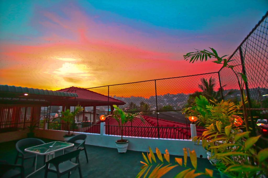 einen Sonnenuntergang auf einem Balkon mit Tischen und Stühlen in der Unterkunft Kandyan Fo Rest in Kandy
