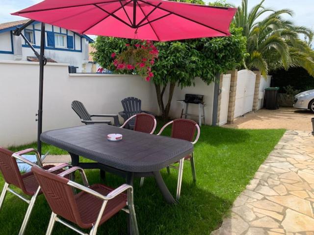 アンダイエにあるAPPARTEMENT LES HIRONDELLES 2KM PLAGE-WiFI-JARDIN-PARKING-DRAPS ET SERVIETTESの黒いテーブルと椅子(ピンクの傘付)