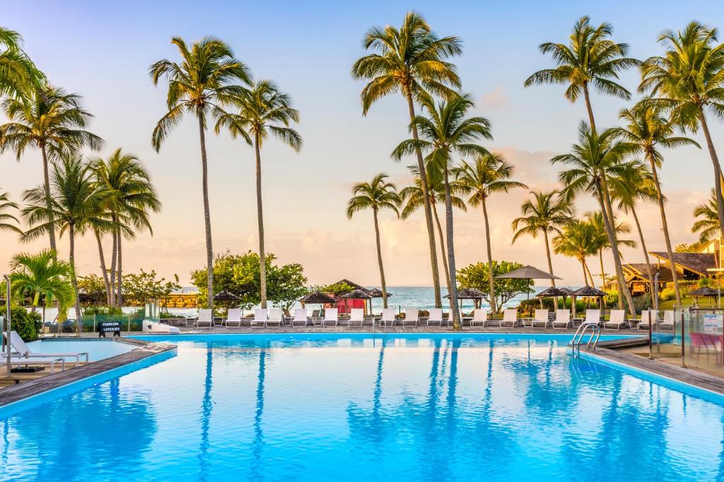 una piscina con palmeras y el océano en La Creole Beach Hotel & Spa en Le Gosier