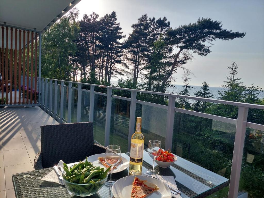 a table with a bottle of wine and vegetables on a balcony at Apartament BalticHoff w Let's Sea Baltic Park Gąski in Gąski