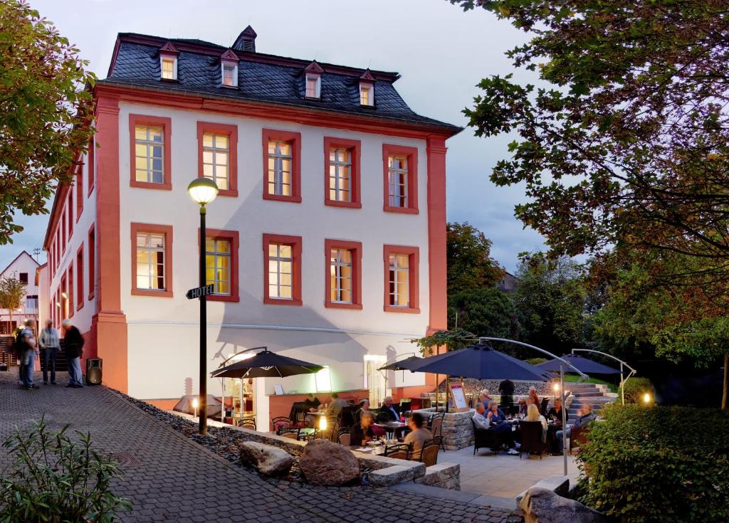 um grande edifício com pessoas sentadas debaixo de guarda-chuvas à sua frente em Hotel Lekker em Neumagen-Dhron