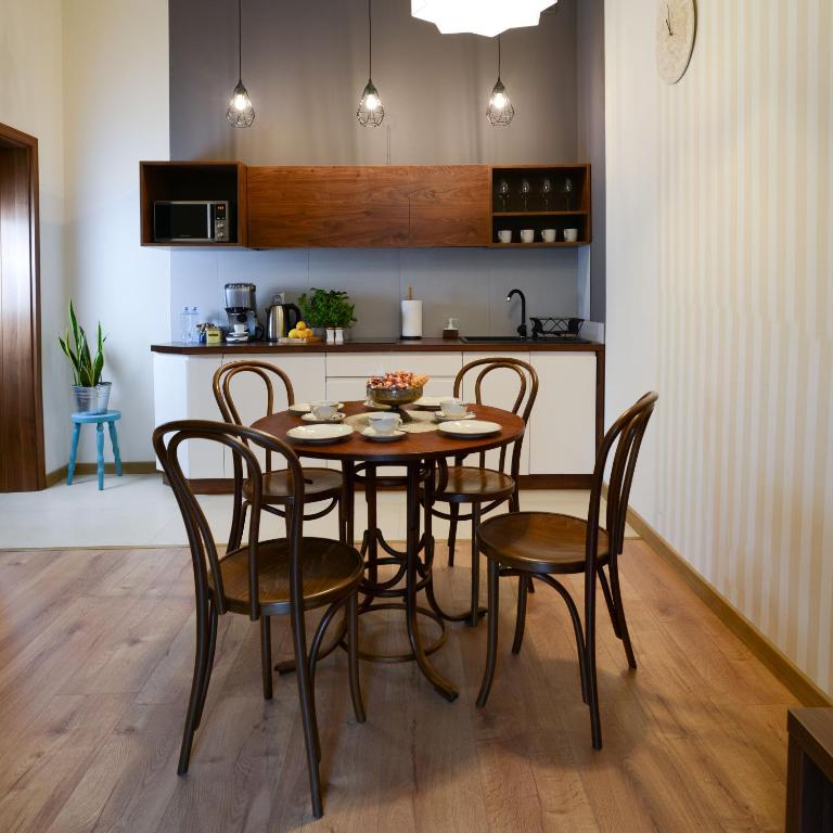 Cozy dining area with round wooden table set for four, pendant lights, and kitchenette background