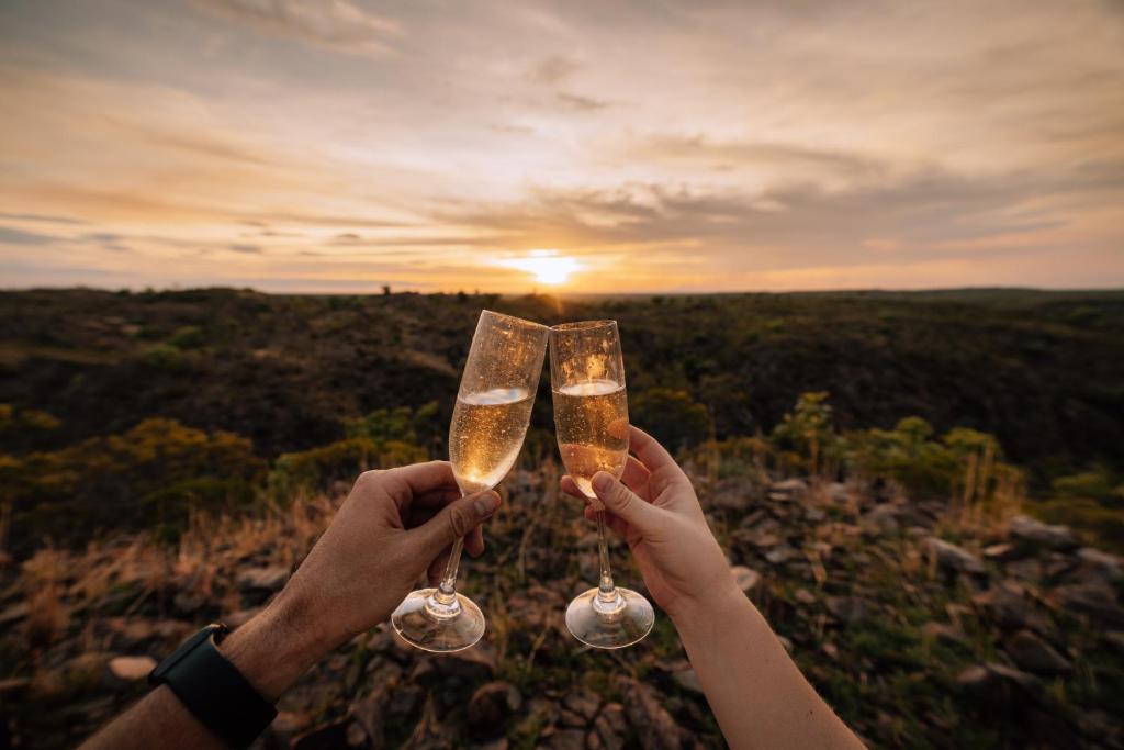 Due persone che portano bicchieri di champagne davanti al tramonto di Gorge View Bush Retreat : Katherine NT a Katherine