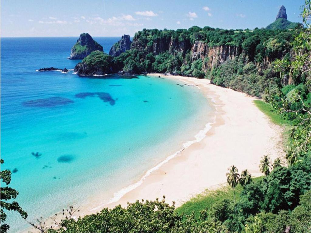 vista su una spiaggia con acqua blu e alberi di Hospedaria Casa dos Gêmeos- Fernando de Noronha-PE a Fernando de Noronha
