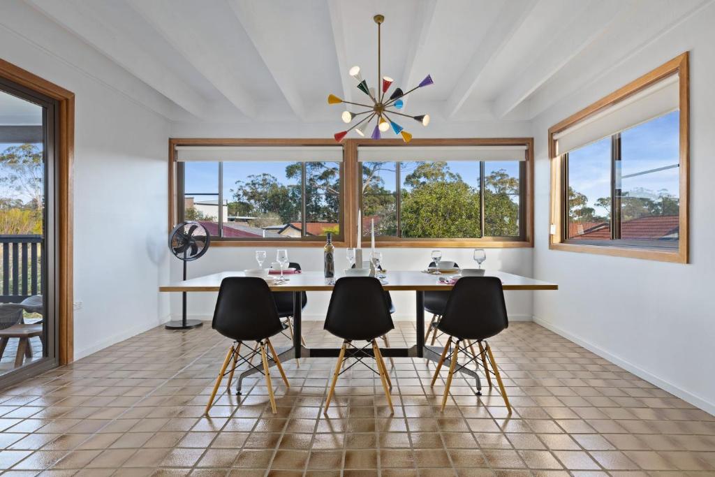 a dining room with a table and chairs and windows at Sputnik Beach House by Experience Jervis Bay in Vincentia