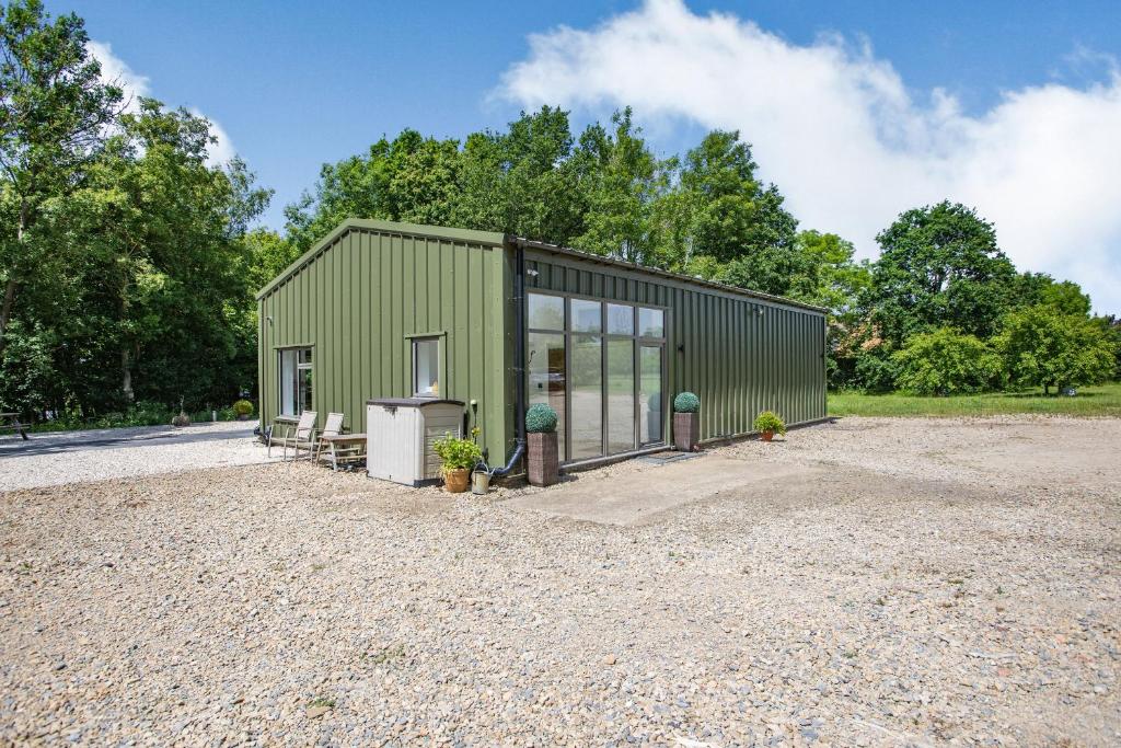 a green building with a stove in a gravel lot at Thatchers Barn in Cheltenham