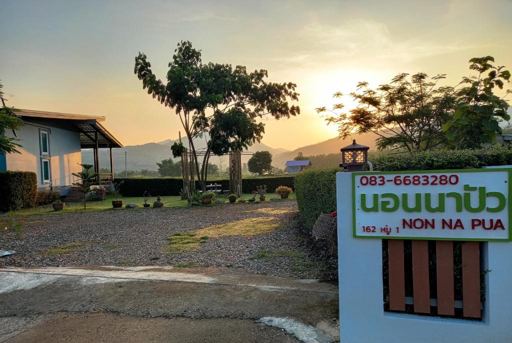 ein Schild vor einem Haus mit Sonnenuntergang im Hintergrund in der Unterkunft NON NA PUA - นอนนา ปัว in Pua