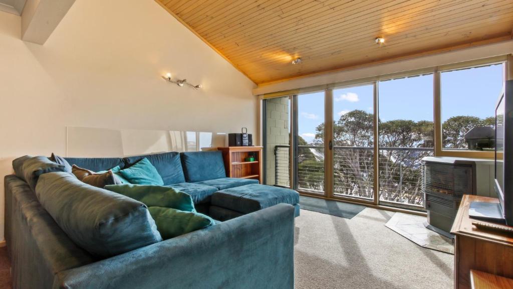 a living room with a blue couch and large windows at Razorback 7 in Mount Hotham