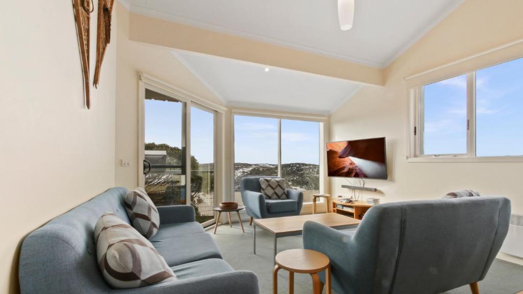 a living room with a blue couch and chairs and windows at Razorback 8 in Mount Hotham